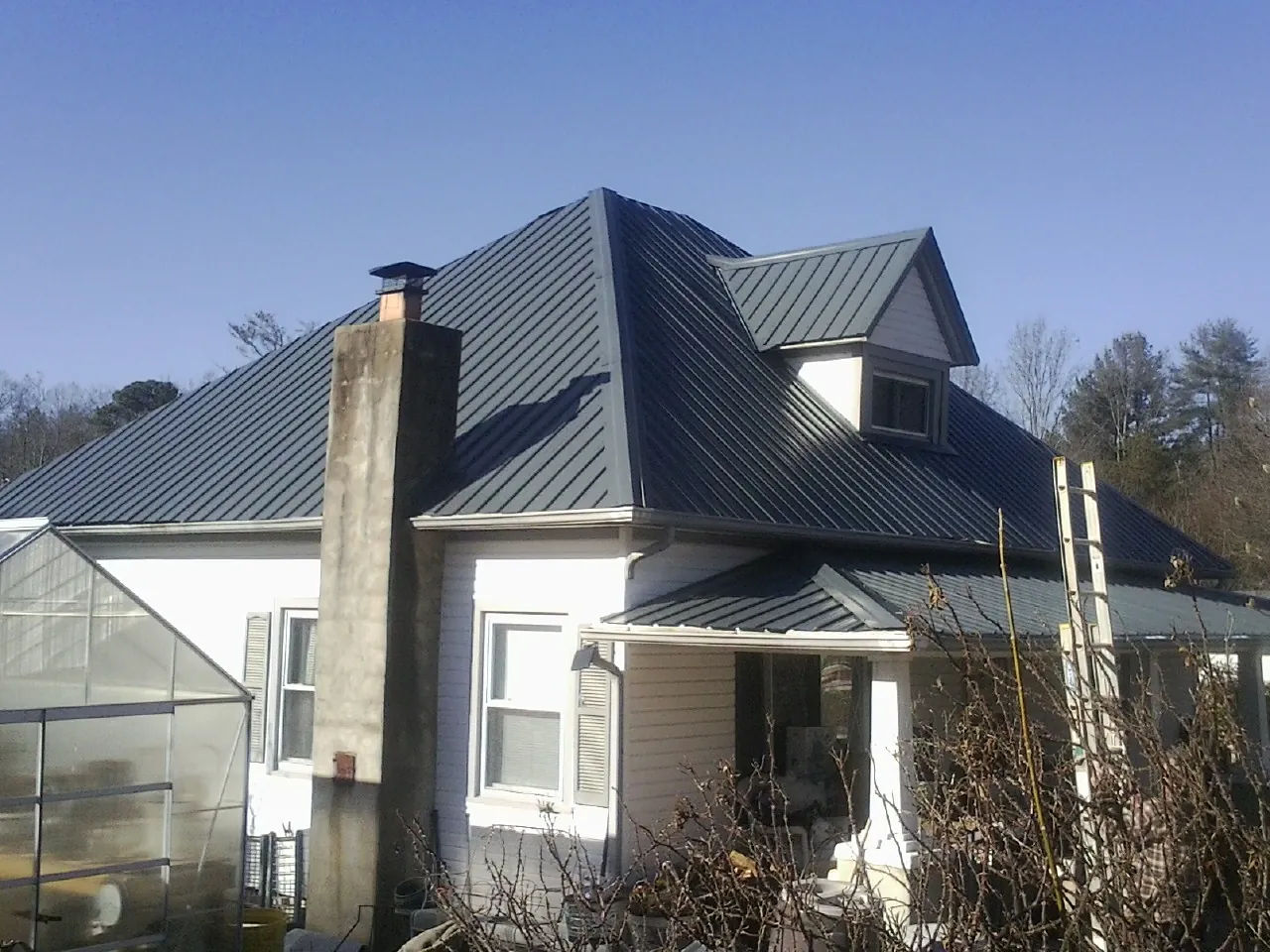 Dark blue standing seam metal roof on a white farmhouse with dormer — Slate & Tile Roof Repair by Roofing Brothers in La Crescent