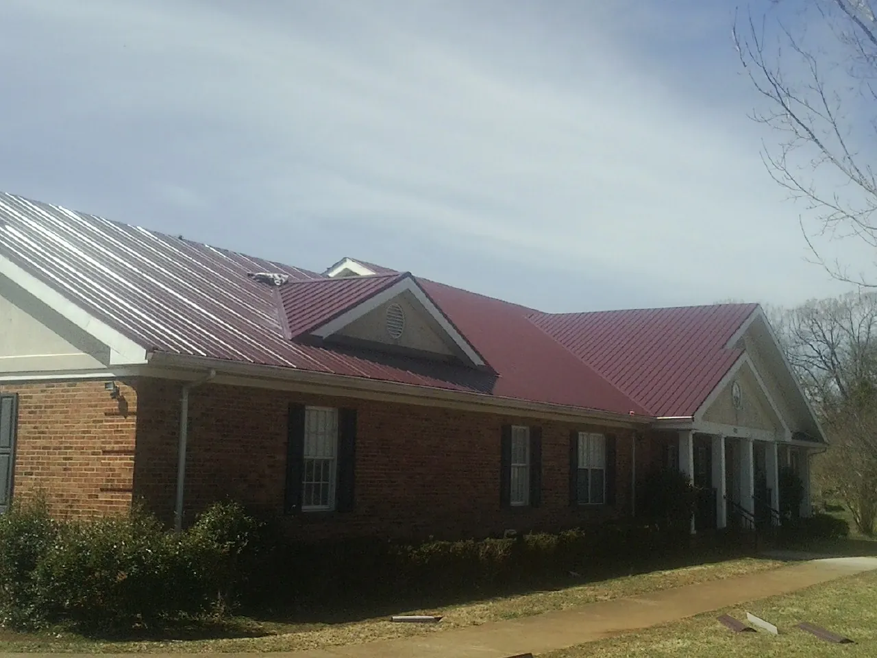 Red metal roof with gabled entries on a long brick building, from a Hail Damage Roof Repair job in La Crescent