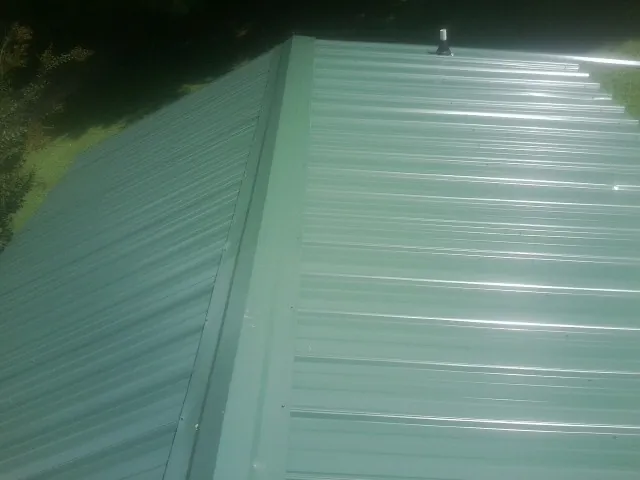 New green metal panels meeting at the ridge of a roof — Flat Roof Repair work by our crew in La Crescent
