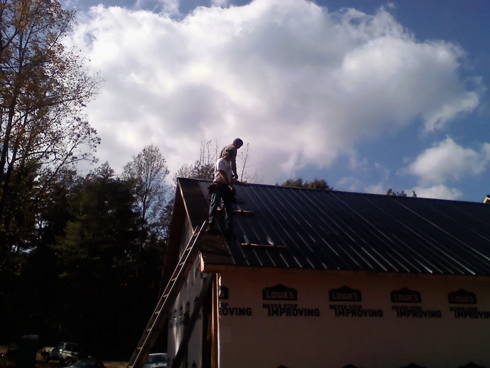Roofer fastening dark metal panels high against a cloudy sky, from a Roof Inspection job in La Crescent