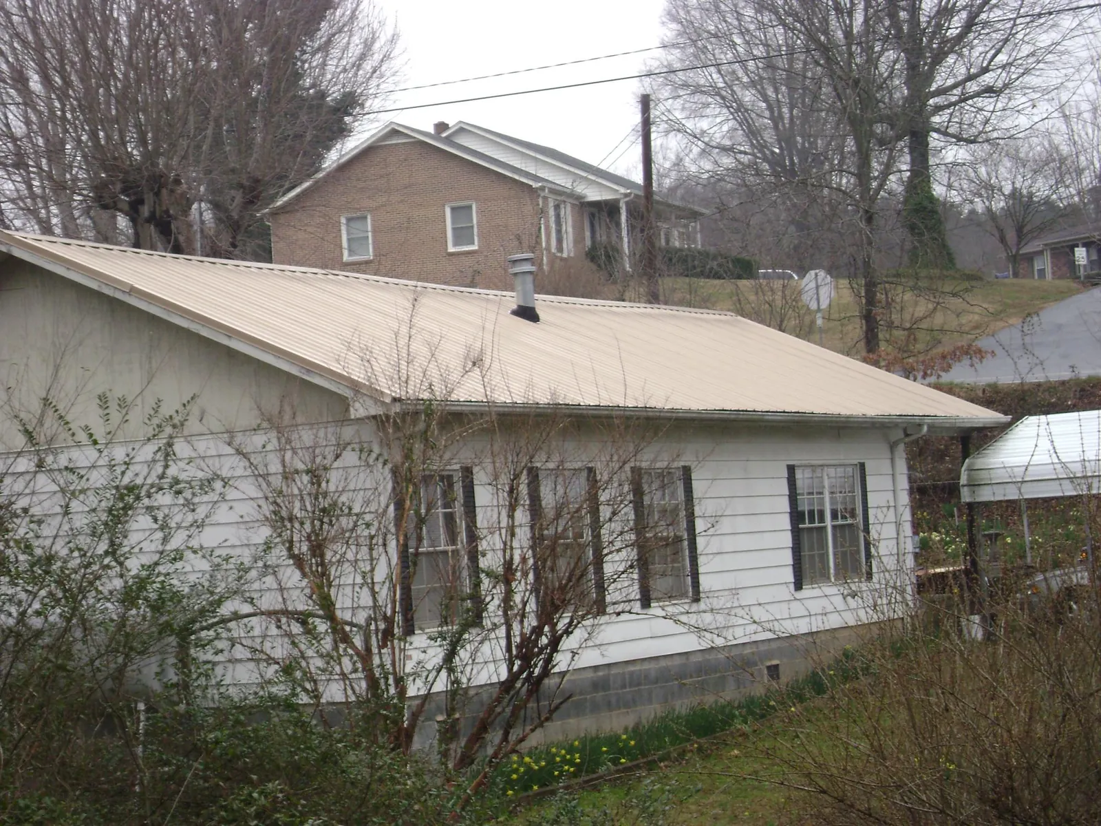 Tan metal roof on a white sided house set into a hillside — Commercial Roofing by Roofing Brothers in La Crescent